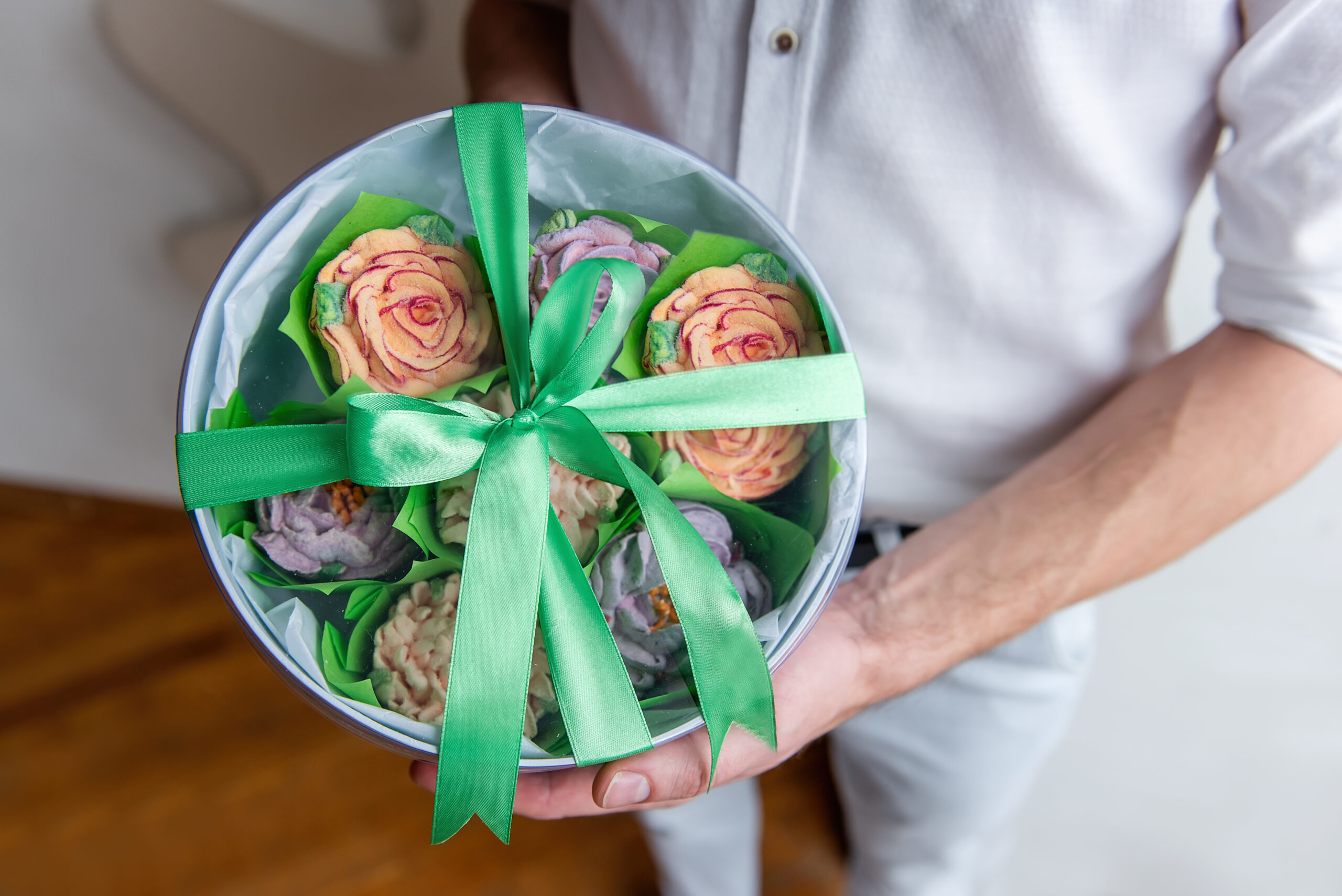 Faceless man holds round box of marshmallow sweet flowers in hands. Gift with green ribbon. Delicate sugarless roses. Small business at home. Hobby baking. Holiday gift. Handmade present. Womens day