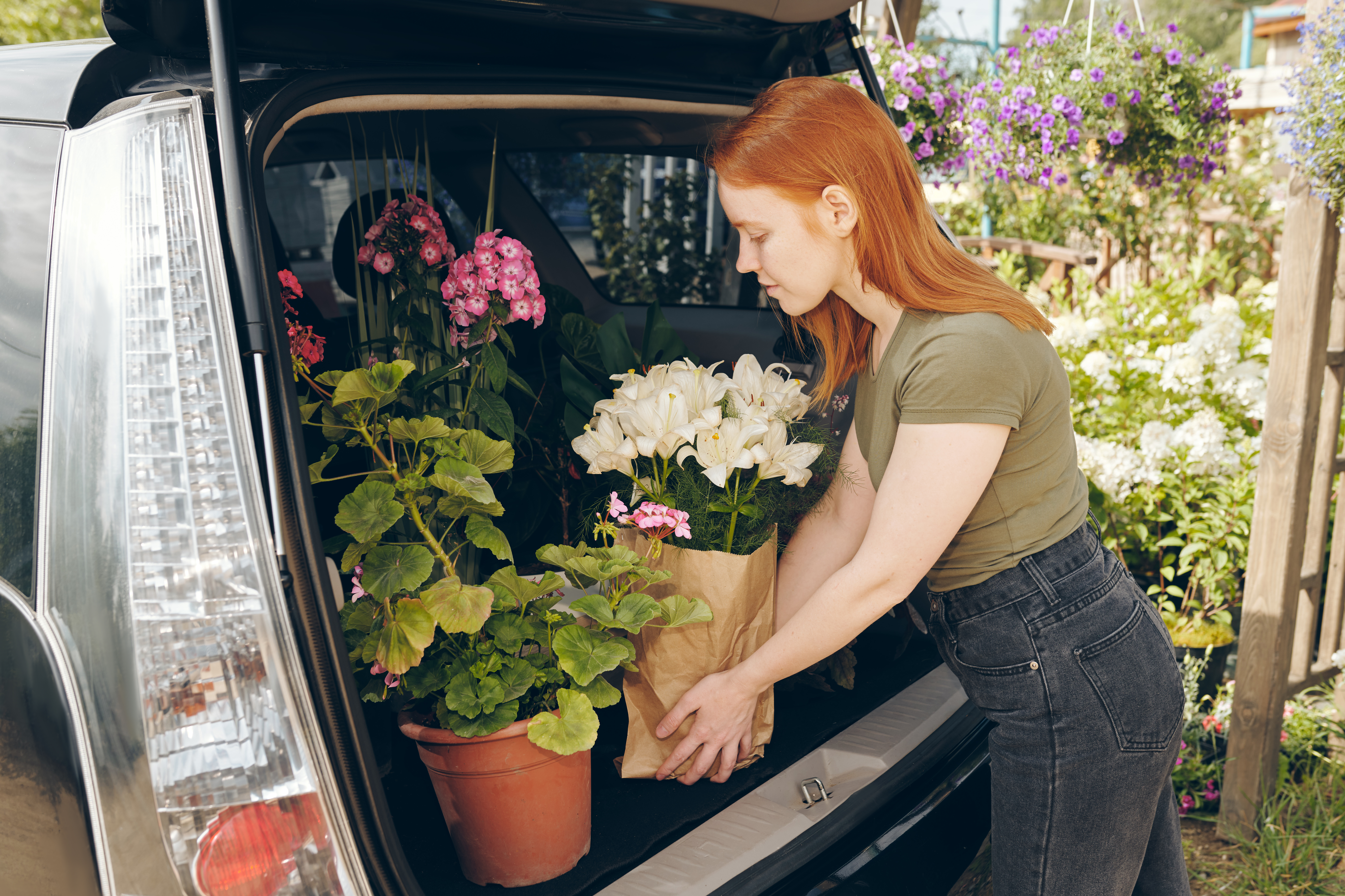 Young flower shop owner packing flowers in car trunk by greenhouse while transporting flowers to store